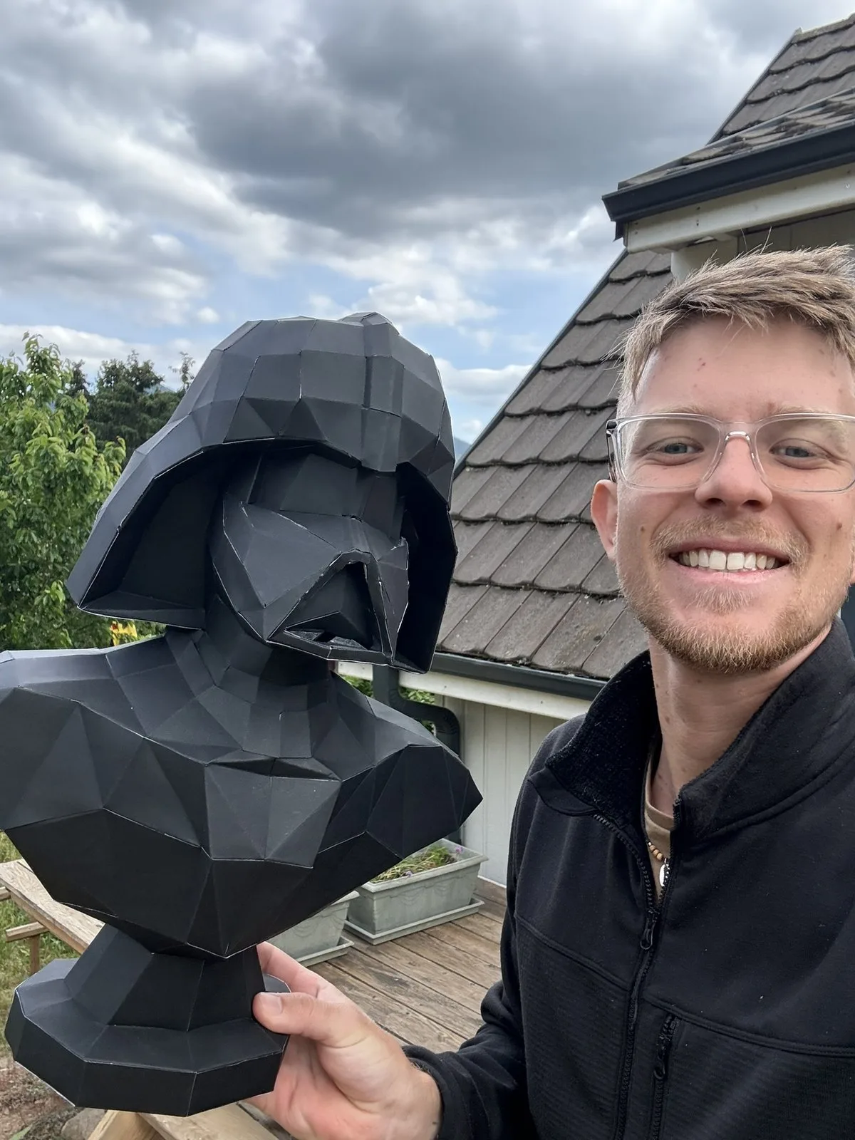 Homme souriant présentant buste de Dark Vador en extérieur