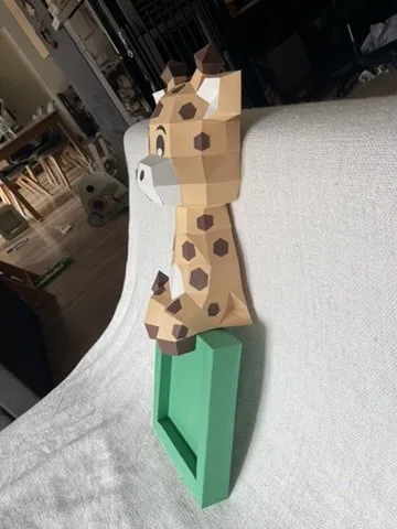 Girafe en papier penchée au-dessus d’un cadre vert