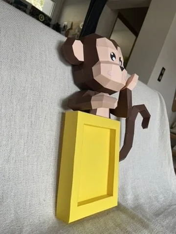 Singe en papier marron accroché à un cadre jaune