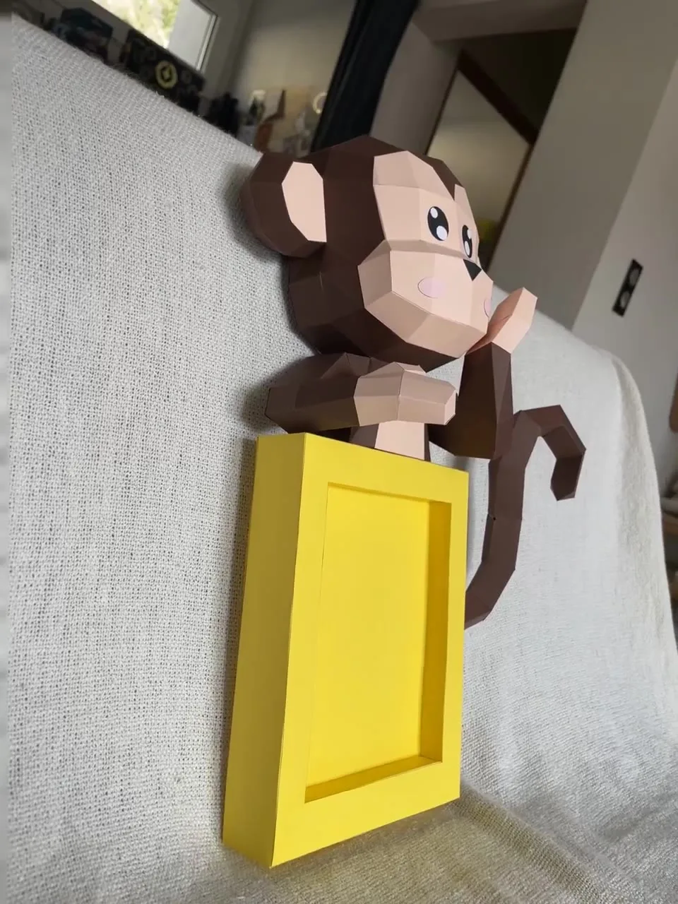 Singe cartoon marron posé sur un cadre photo jaune
