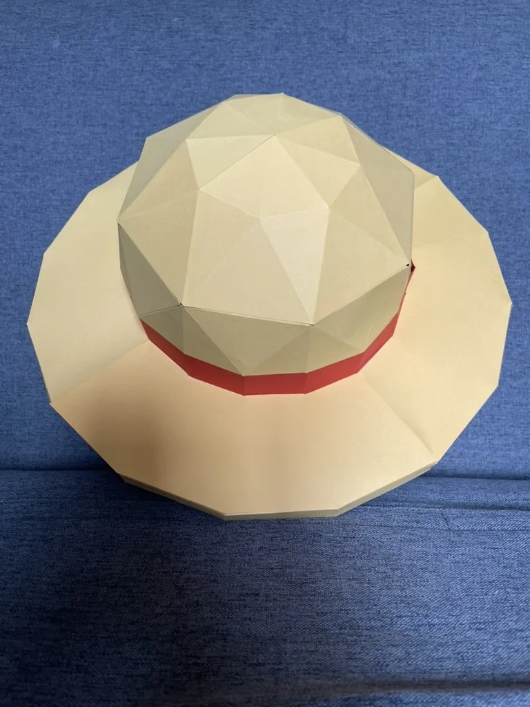 Chapeau de Luffy beige à ruban rouge posé sur une surface claire