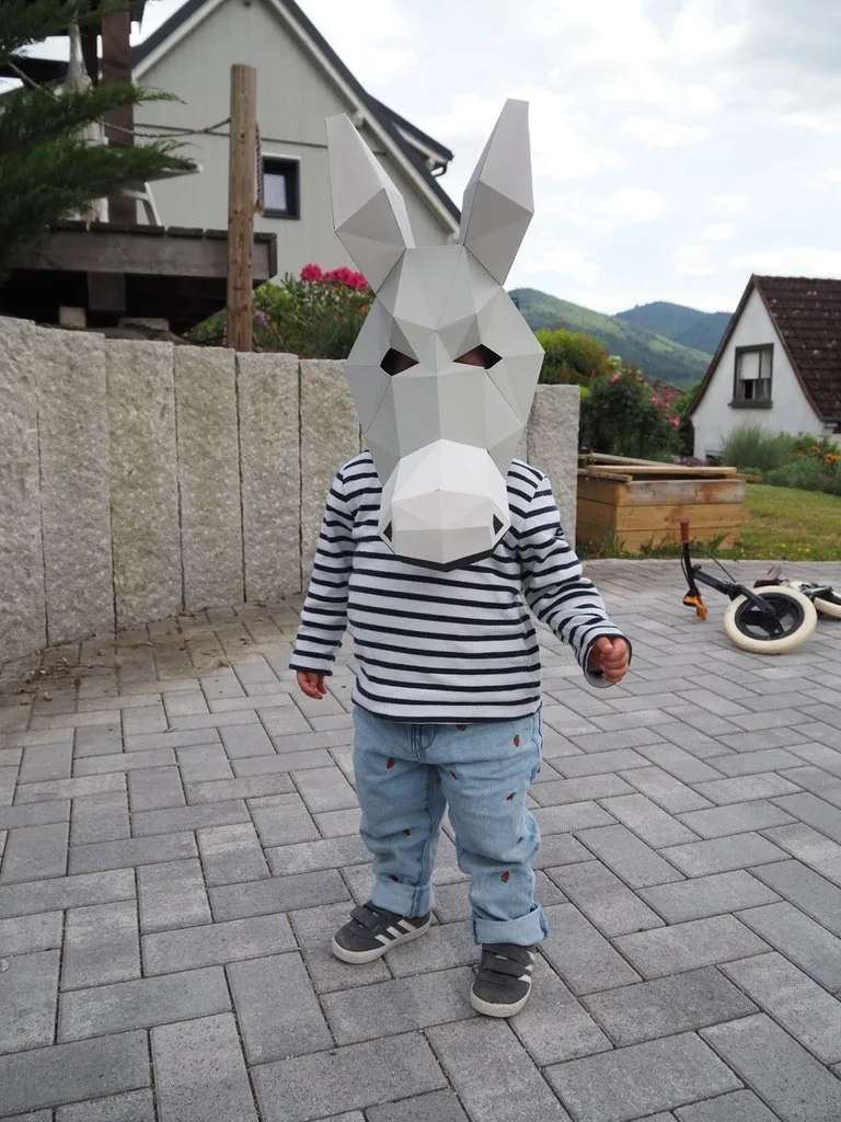 Enfant souriant avec masque d’âne gris dans un jardin ensoleillé