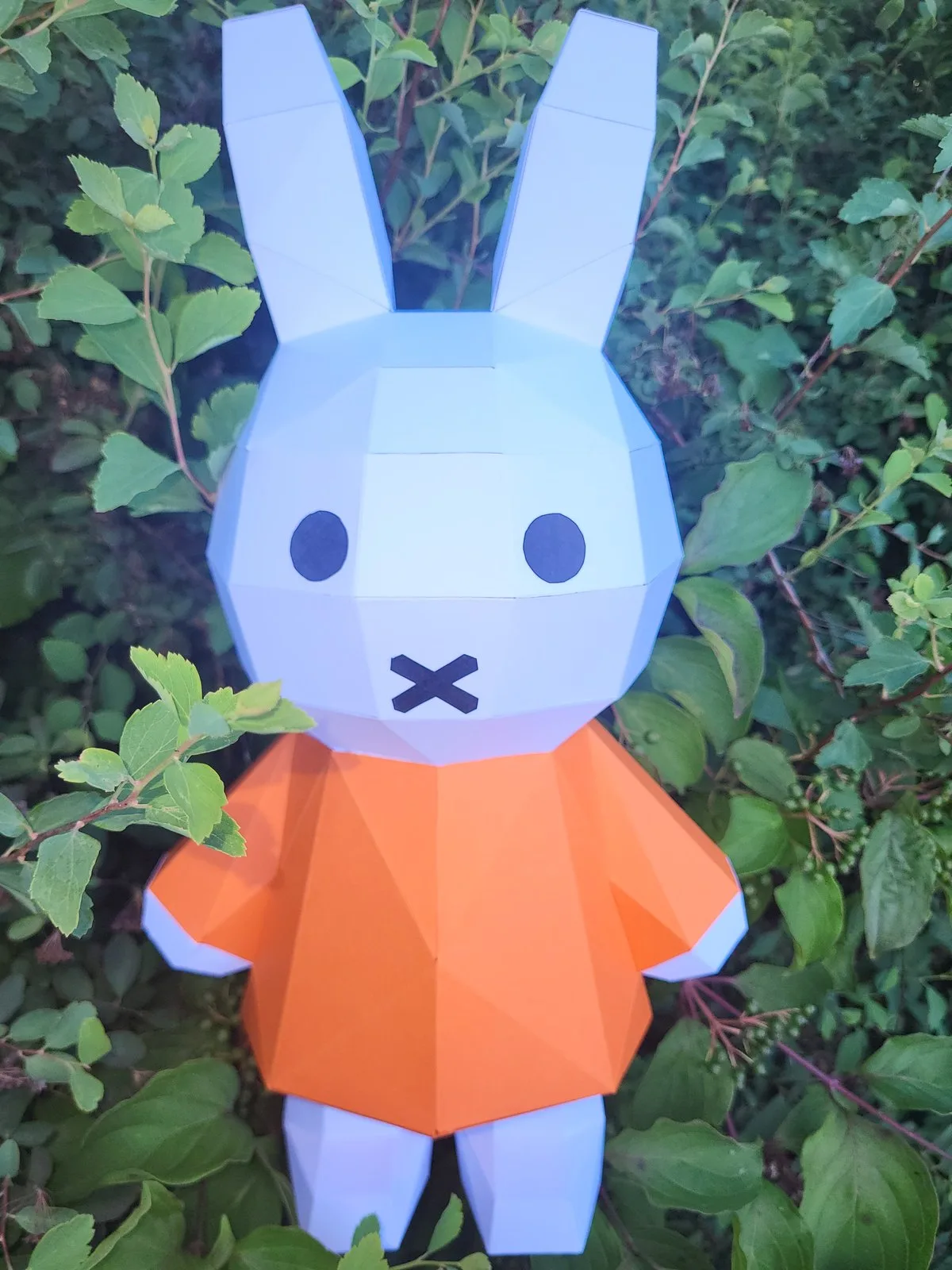 Lapin Miffy en papercraft tenu devant des feuilles vertes