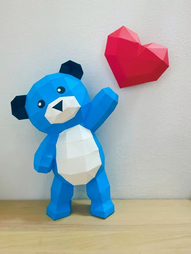 Ours bleu en papier levant un bras près d’un cœur rouge