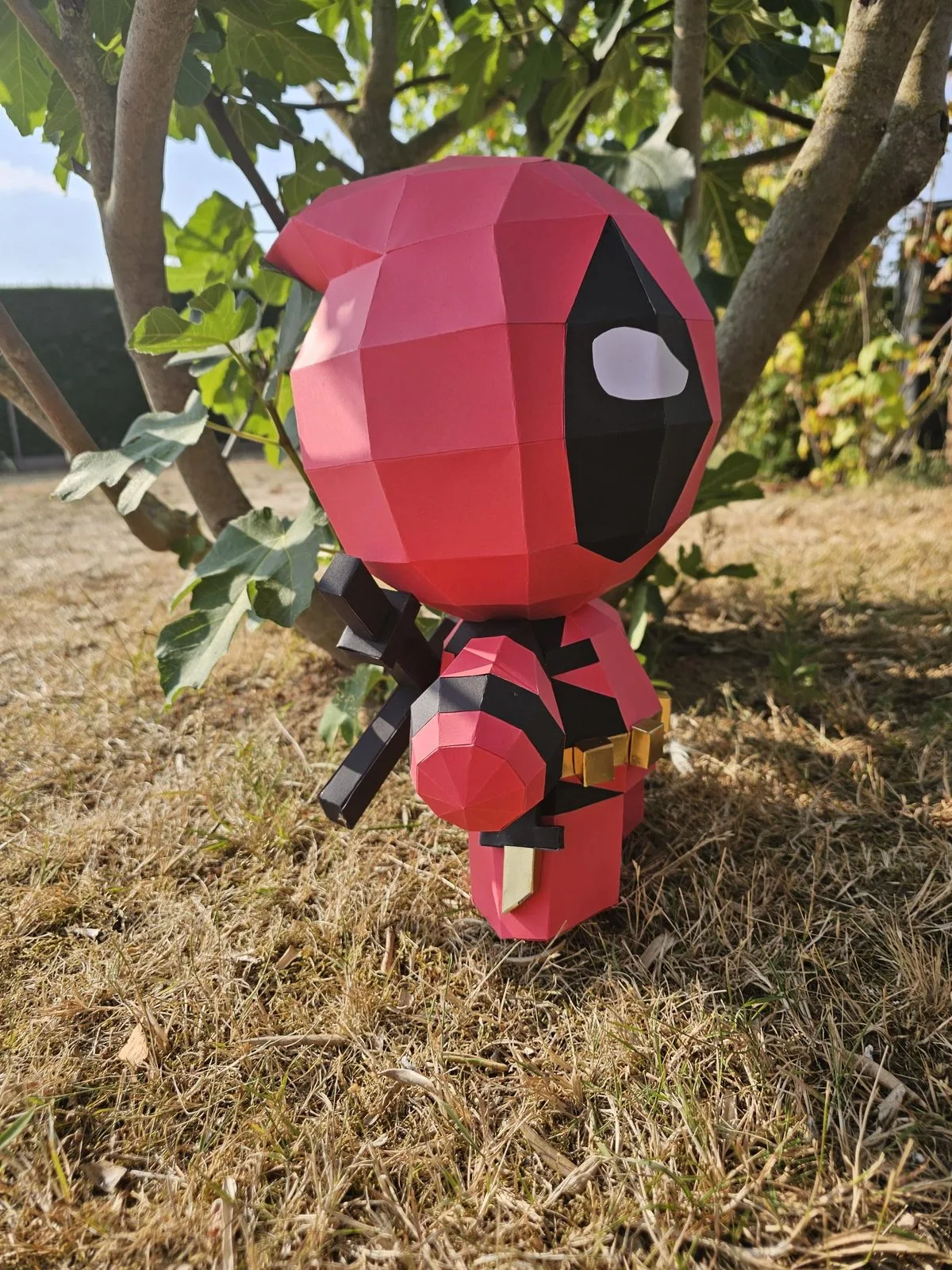 Bébé Deadpool en papercraft debout dans l'herbe sèche