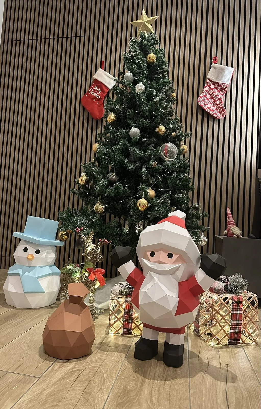 Scène de Noël : Père Noël bras levés moufles noires, bonhomme de neige chapeau bleu, hotte marron de