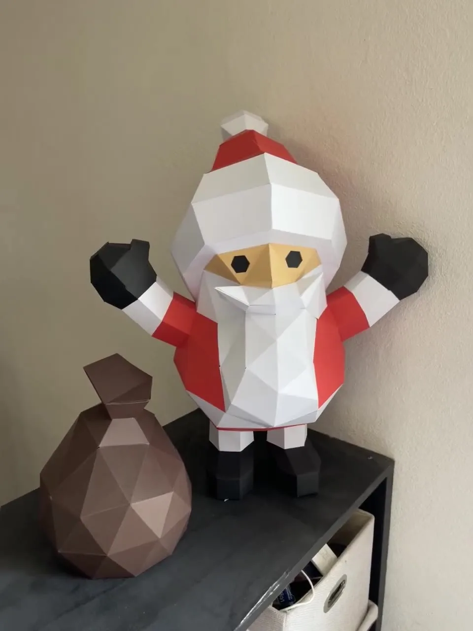 Père Noël papercraft assemblé bras levés avec sac marron sur un meuble