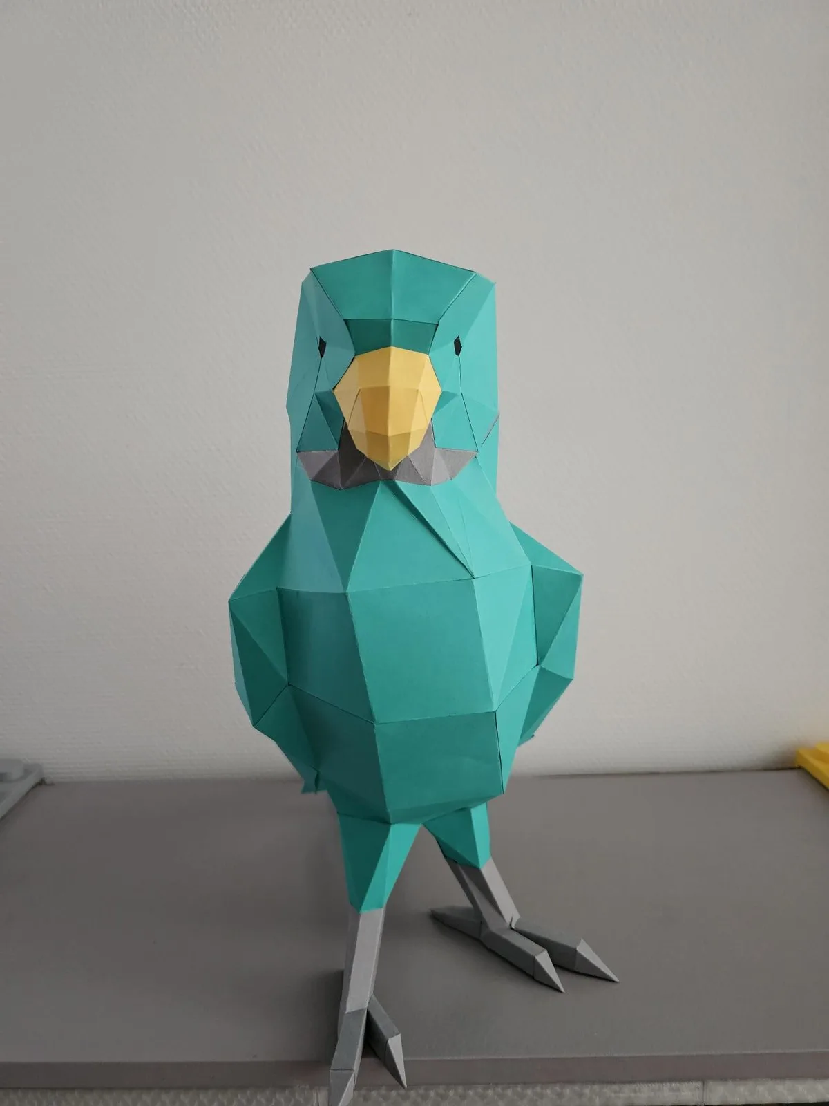 Perroquet vert en papercraft posé sur un plan de travail clair