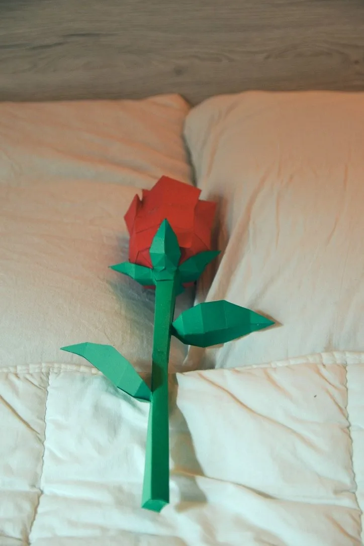 Rose en papercraft rouge posée délicatement sur un lit