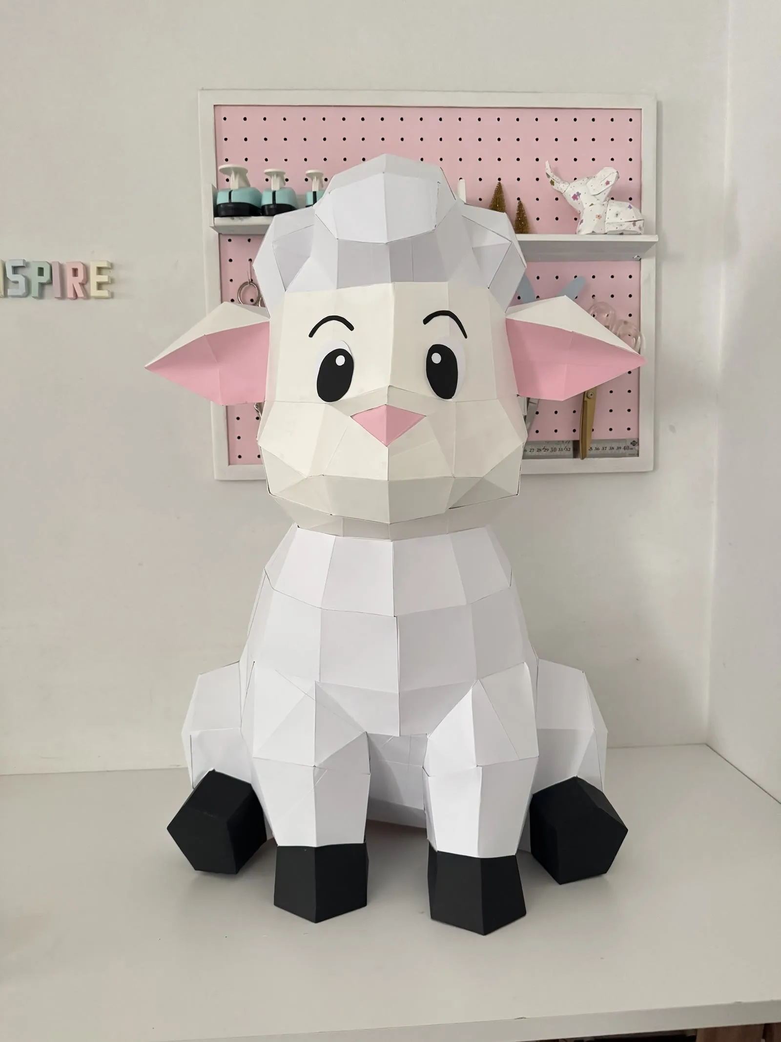 Mouton assis en papercraft 3D vu de face avec une variante de visage aux yeux souriants, monté en papier blanc