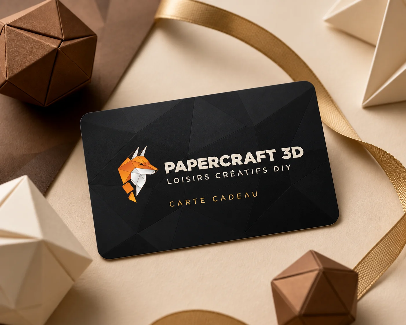 Carte cadeau noire avec le logo renard orange et blanc Papercraft 3D, entourée de créations en papier et d’un ruban doré